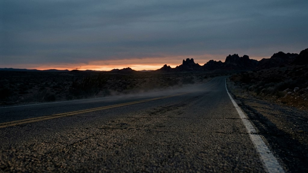 Cinematic still of a desert road at dusk with a thin haze of dust catching low light
